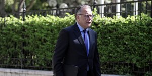 Ο Γιώργος Κουμουτσάκος με μπλε πουκάμισο, περπατά με έναν φάκελο στα χέρια