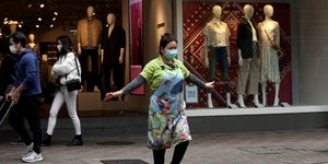 Γυναίκα με ιατρική μάσκα σε διάβαση, απλώνει τα χέρια της