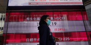 Γυναίκα με μάσκα περνά μπροστά από το χρηματιστήριο του Χονγκ Κονγκ 