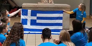 Μαθητές κάθονται οκλαδόν μπροστά από την Καρυάτιδα στο Βρετανικό Μουσείο, κρατώντας την ελληνική σημαία