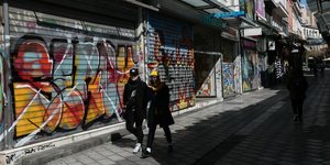 Ζευγάρι μπροστά από κλειστά ρολά καταστημάτων λόγω κορωνοϊού