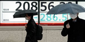 Ανδρες με ιατρική μάσκα και ομπρέλα περνούν μπροστά από οθόνη