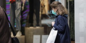 γυναίκα με μάσκα μπροστά από βιτρίνες