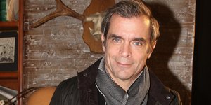 Ο Κωνσταντίνος Μαρκουλάκης με φουλάρι γκρι κρατάει μια σαμπάνια