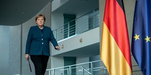 Η Ανγκελα Μέρκελ περπατά δίπλα από σημαίες Γερμανίας και ΕΕ