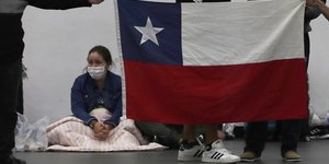 Γυναίκα στο πάτωμα με κουβέρτα και μάσκα, μπροστά από σημαία της Χιλής