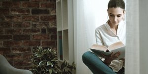 Γυναίκα διαβάζει βιβλίο μπροστά στο παράθυρο του σπιτιού