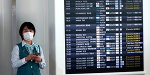 Υπάλληλος με μάσκα δίπλα από πίνακα με ώρες αφίξεων πτήσεων