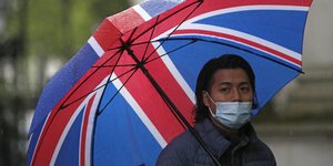 Άνδρας με ομπρέλα στα χρώματα της Βρετανίας και μάσκα προστασίας από τον κορωνοϊό