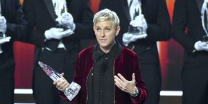 Η Ελεν Ντε Τζένερις κρατάει βραβείο και φοράει μπορντώ πανωφόρι