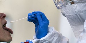 Γιατρός με στολή, μάσκα και γάντια πραγματοποιεί τεστ για τον κορωνοϊό με τη μέθοδο του επιχρίσματος