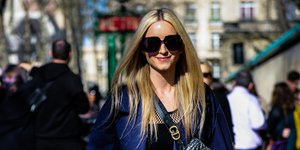 Γυναίκα περπατάει με μπλε σακάκι και γυαλιά ηλίου