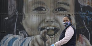 Γυναίκα στην Κολομβία με μαντήλι στο πρόσωπο και γάντια, μπροστά από ένα τεράστιο γκράφιτι ενός παιδιού που γελά