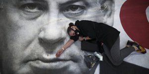 Γυναίκα συμμετέχει σε διαμαρτυρία στο Τελ Αβίβ, ξαπλωμένη πάνω σε αφίσα του Μπενιαμίν Νετανιάχου