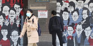 Γυναίκα με μάσκα περπατά έξω από κατεβασμένα ρολά στην Ιαπωνία