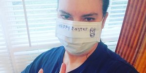 Γυναίκα με μάσκα λόγω κορωνοϊού που γράφει καλό Πάσχα