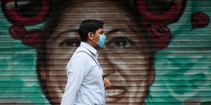 Μεξικανός περνά μπροστά από γκράφιτι φορώντας μάσκα