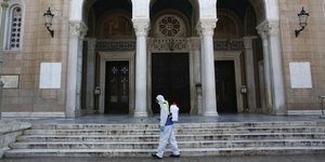 Εξωτερική όψη της Μητρόπολης Αθηνών, ενώ άνδρας του Δήμου Αθηναίων απολυμαίνει τον χώρο