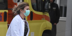 Νοσοκόμα περνά μπροστά από ασθενοφόρο φορώντας μάσκα