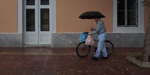 Ηλικιωμένος με ομπρέλα κουβαλάει ποδήλατο και τσάντες