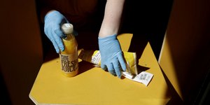 Πωλητής με γάντια μιας χρήσης κρατά ένα μπουκάλι με φυσικό χυμό