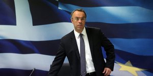 Ο Χρήστος Σταϊκούρας στέκεται όρθιος μπροστά από την ελληνική σημαία