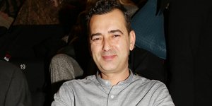 Ο Αγγελος Μπράτης με γκρι πουκάμισο καθισμένος στο θέατρο