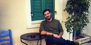 Ο Άκης Πετρετζίκης κάθεται σε μπλε καρέκλα