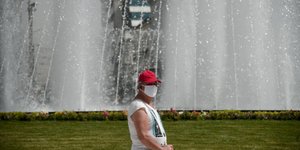 Άνδρας με μάσκα και καπέλο μπροστά σε σιντριβάνι