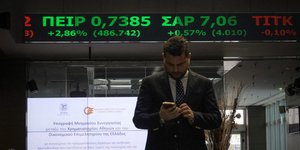 Άνδρας συμβουλεύεται το κινητό του μέσα στο κτίριο του Χρηματιστηρίου Αθηνών