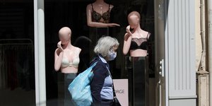 Γυναίκα με μάσκα προστασίας από τον κορωνοϊό μπροστά από βιτρίνα με πλαστικές κούκλες στο Παρίσι