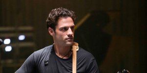 Ο Κωνσταντίνος Αργυρός ξυρισμένος κρατά μια κιθάρα
