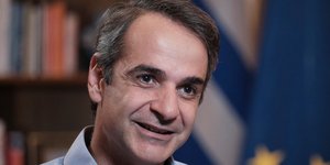 Ο Κυριάκος Μητσοτάκης χαμογελαστός, με γαλάζιο πουκάμισο