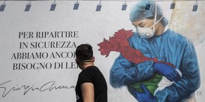 Άνδρας μπροστά από πανό στο Μιλάνο, όπου νοσοκόμα κρατά την Ιταλία στην αγκαλιά της