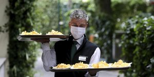 Σερβιτόρος με δύο δίσκους στα χέρια και μάσκα προστασίας από τον κορωνοϊό στην Αυστρία