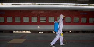 Άνδρας με στολή, γάντια και μάσκα απολυμαίνει αποβάθρα τρένου