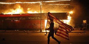 Άνδρας με την αμερικανική σημαία διαδηλώνει στη Μινεάπολη μπροστά από φωτιές