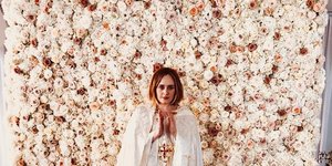 Η Αντέλ με λευκά, μπροστά από έναν τοίχο από άσπρα λουλούδια