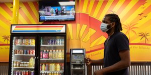 Αφροαμερικανός με μάσκα για κορωνοϊό περνά μπροστά από ψυγείο με ροφήματα