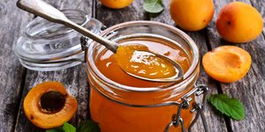 Βάζο με σπιτική μαρμελάδα βερίκοκο, πλάι σε διάσπαρτα φρούτα