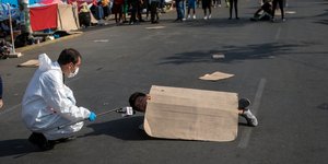 Δημοσιογράφος με στολή και μάσκα για κορωνοϊό μιλά με διαδηλωτή που ξάπλωσε στο έδαφος