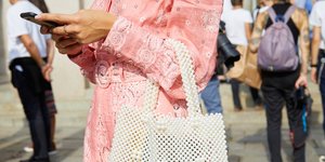 Γυναίκα με ροζ ολόσωμο σορτς και λευκή τσάντα κρατάει κινητό στα χέρια της 