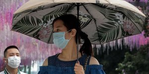 Γυναίκα με ομπρέλα και μάσκα για τον κορωνοϊό στην Κίνα