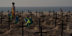 Γυναίκα με μάσκα κοιτάζει σταυρούς στο χώμα δίπλα σε παραλία