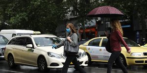 Γυναίκες περνούν διάβαση μπροστά από ταξί, στην βροχή