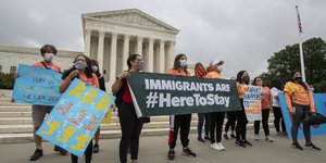 Διαδηλωτές κρατούν πανό που γράφει «οι μετανάστες είναι εδώ για να μείνουν» 