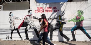 Νεαροί περνάνε από τοίχο με γκράφιτι που έχει γιατρούς, Μπολσονάρου και κορωνοϊό