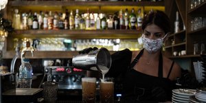 Σερβιτόρα ετοιμάζει καφέδες φορώντας μάσκα για τον κορωνοϊό