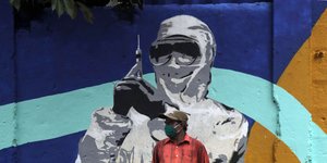 Γκράφιτι άνδρα με στολή και μάσκα να κρατά εμβόλιο κατά του κορωνοϊού