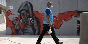 άνδρας με μάσκα περπατά μπροστά από γκράφιτι